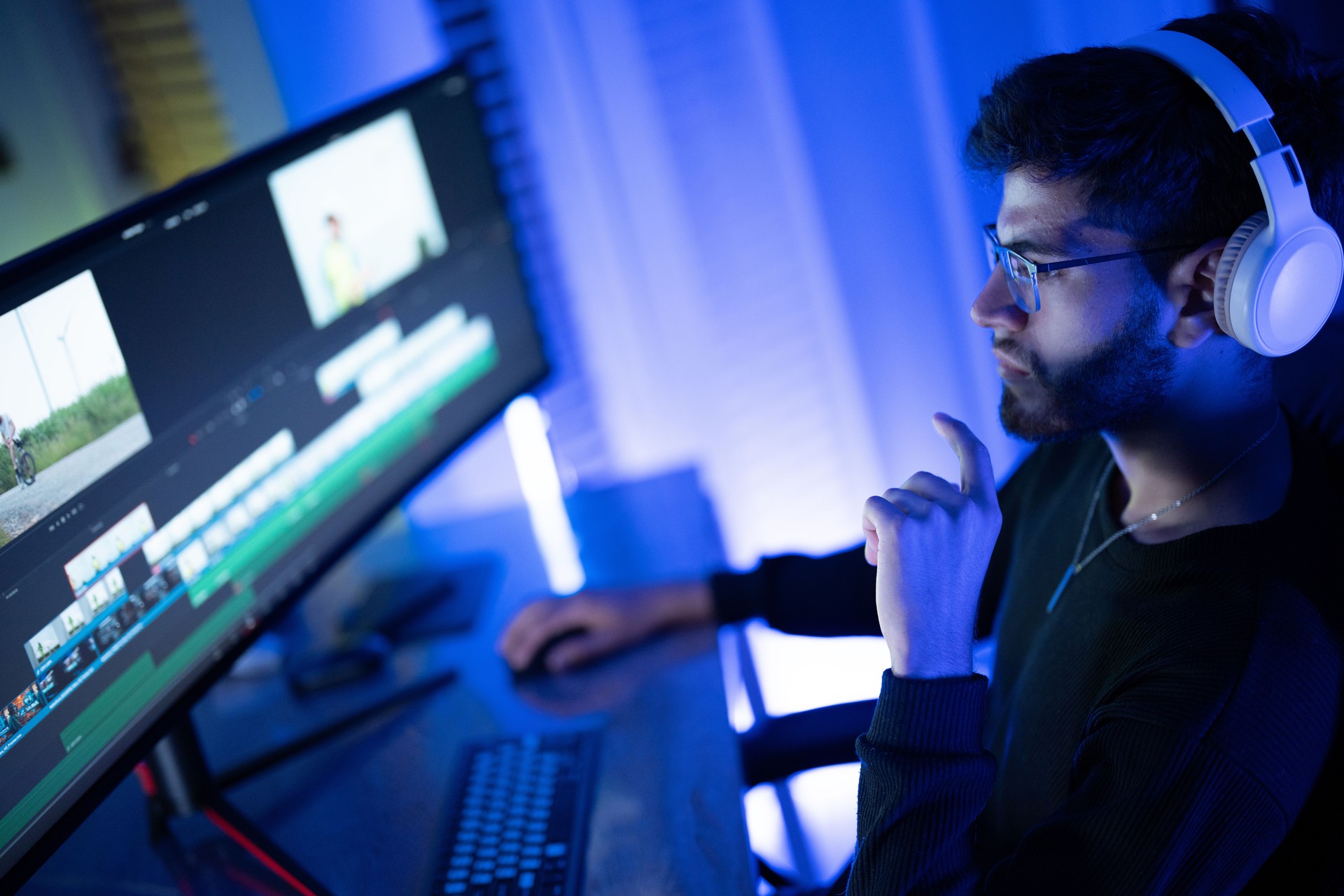 Young man engaged in video editing at a modern workstation surrounded by blue lighting