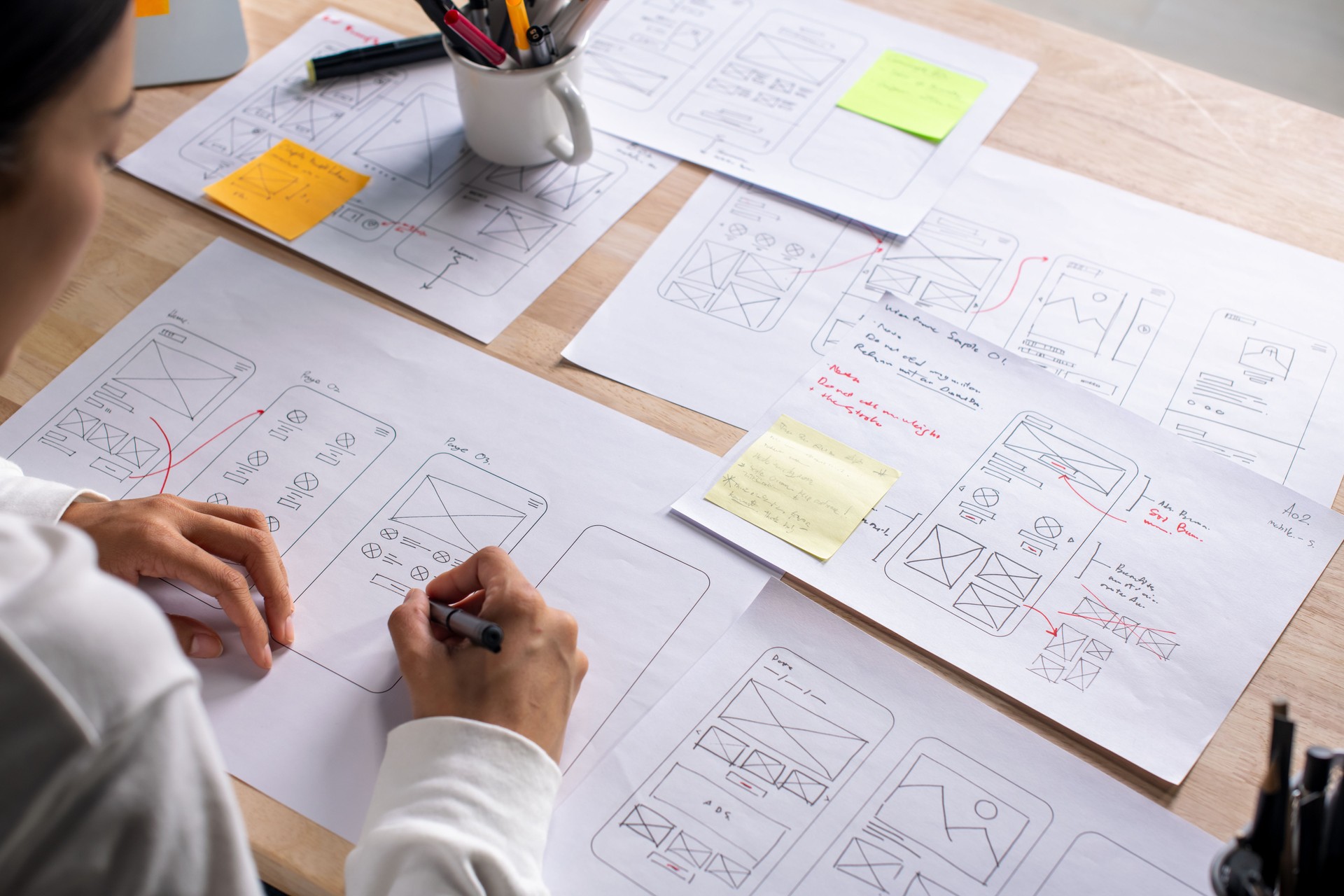 UX UI designer working on wireframes for a website and mobile app prototype, surrounded by sketches of user-flow and design tools, in concept of website and mobile application design concept.